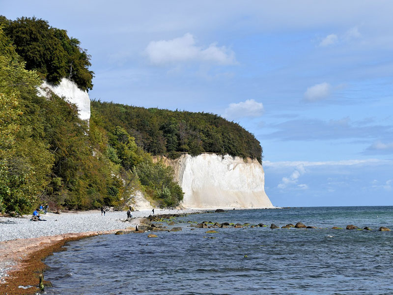 Foto der Kreidefelsen auf Rügen, daneben Kiesstrand mit ein paar Menschen