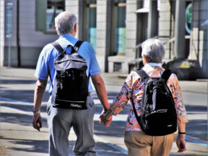 Mann und Frau, grauhaarig, mit Rucksack, gehen Hand in Hand in einer Stadt