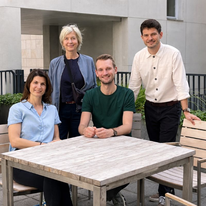 Teamfoto: zwei Frauen, zwei Männer am Holztisch im Innenhof